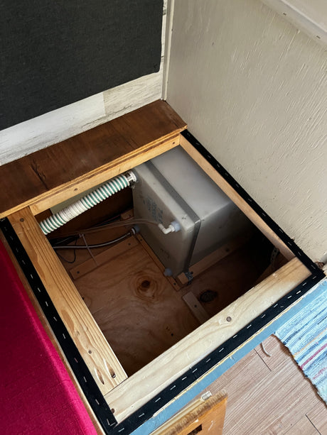 RV rental under-bed storage revealing a freshwater tank, plumbing, and wiring, neatly tucked away for compact living.