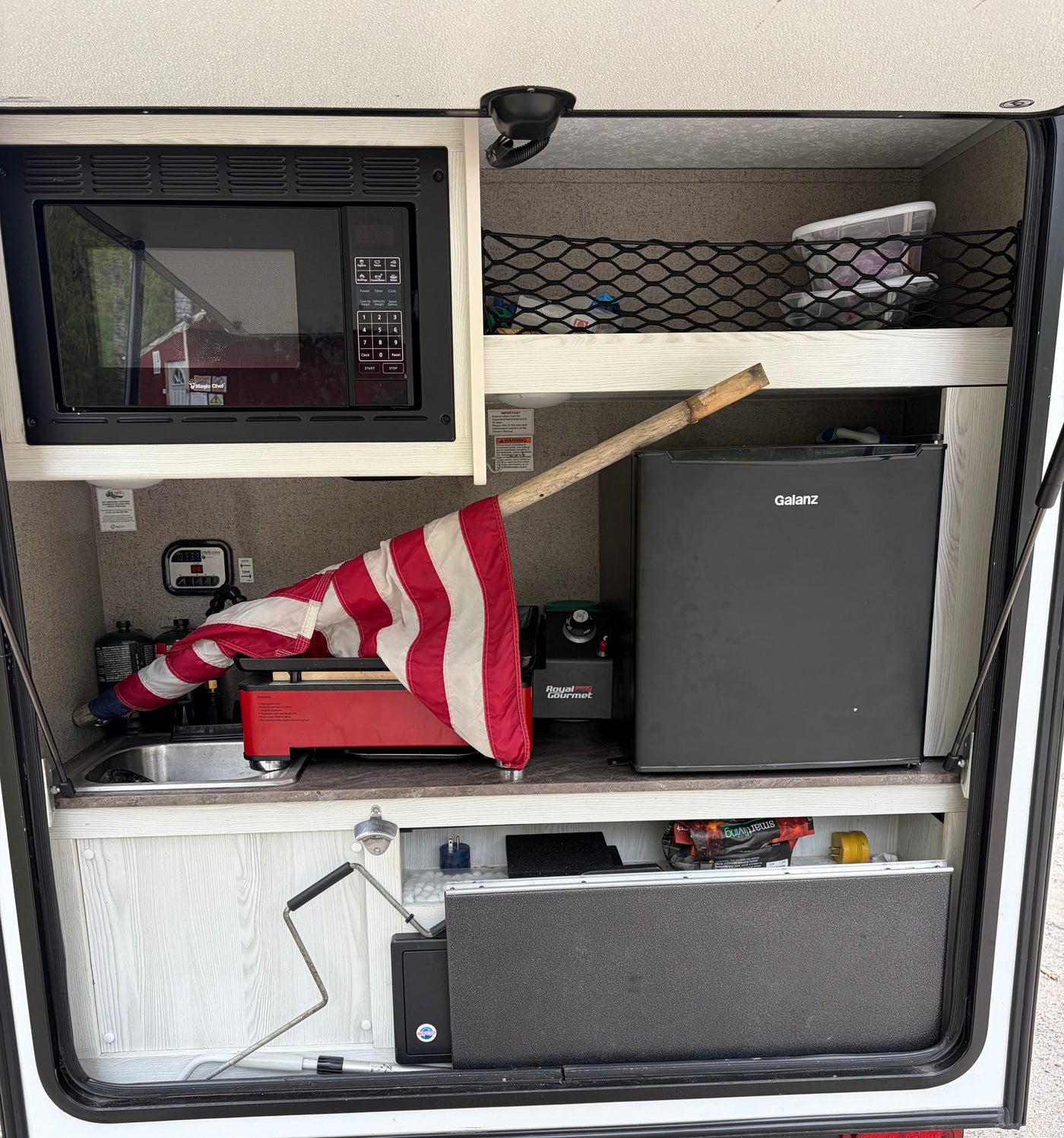 This RV rental kitchen has a microwave, Galanz mini-fridge, sink, Royal Gourmet griddle, and US flag, perfect for compact cooking. — photo 7