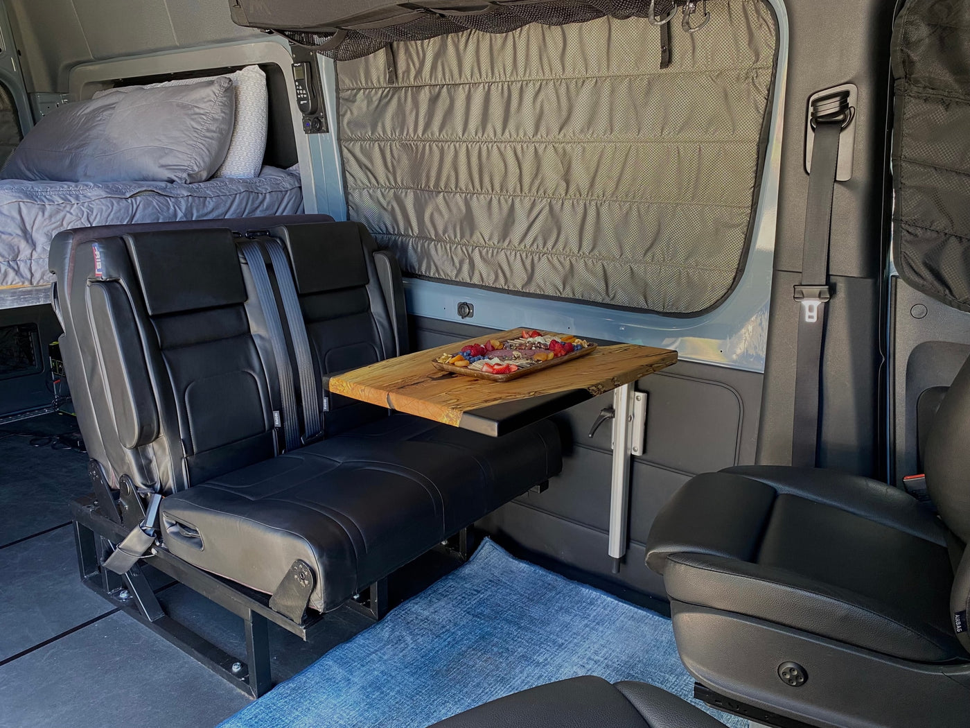This RV rental interior offers a comfy bed, passenger seats, and a wood table laden with snacks, ready for your road trip. — photo 8