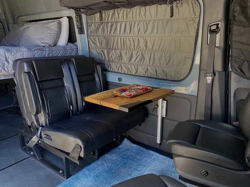 This RV rental interior offers a comfy bed, passenger seats, and a wood table laden with snacks, ready for your road trip. — photo 8
