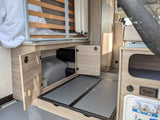 RV rental interior: lifted bed, under-bed storage revealing water tank, & utility hookups for your adventure.