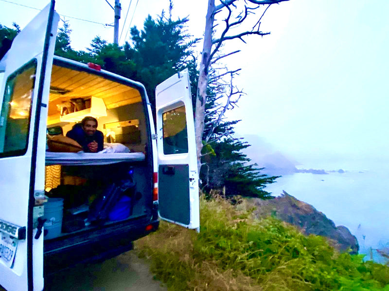 Cozy rv rental experience: A man relaxing inside his campervan, parked overlooking a misty coastal ocean view. — photo 15