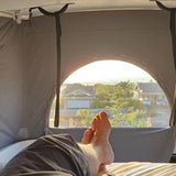 Cozy RV rental pop-top bed view. Relaxing with feet up in a camper van, enjoying the sunny landscape.