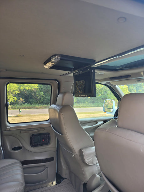 RV rental interior: A spacious conversion van's light-colored leather seating, overhead entertainment screen, and window view.