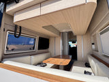 Enjoy this bright RV rental interior featuring light wood, cream seating, a versatile table, and a scenic beach view from the window.