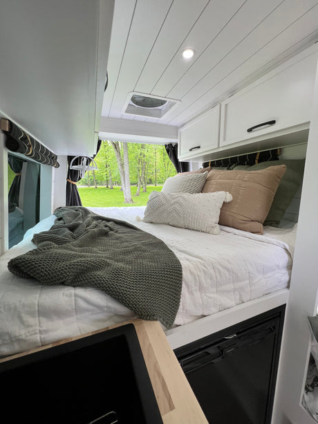 Cozy RV rental bedroom featuring a comfy bed with plush pillows, modern cabinets, and a beautiful nature view.