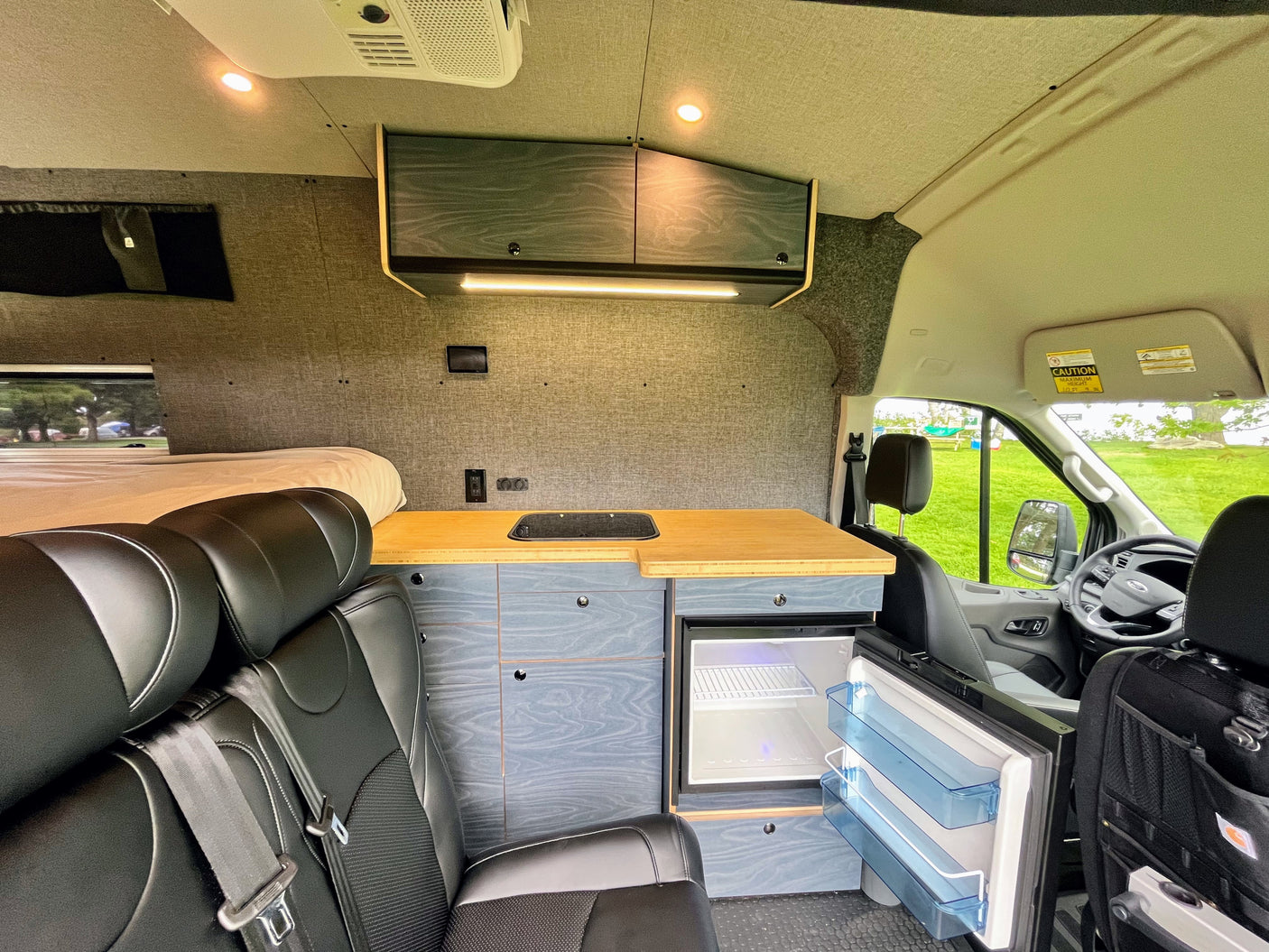 View inside an rv rental: features a bed, compact kitchen, fridge, custom cabinets, and seating, ready for adventure.