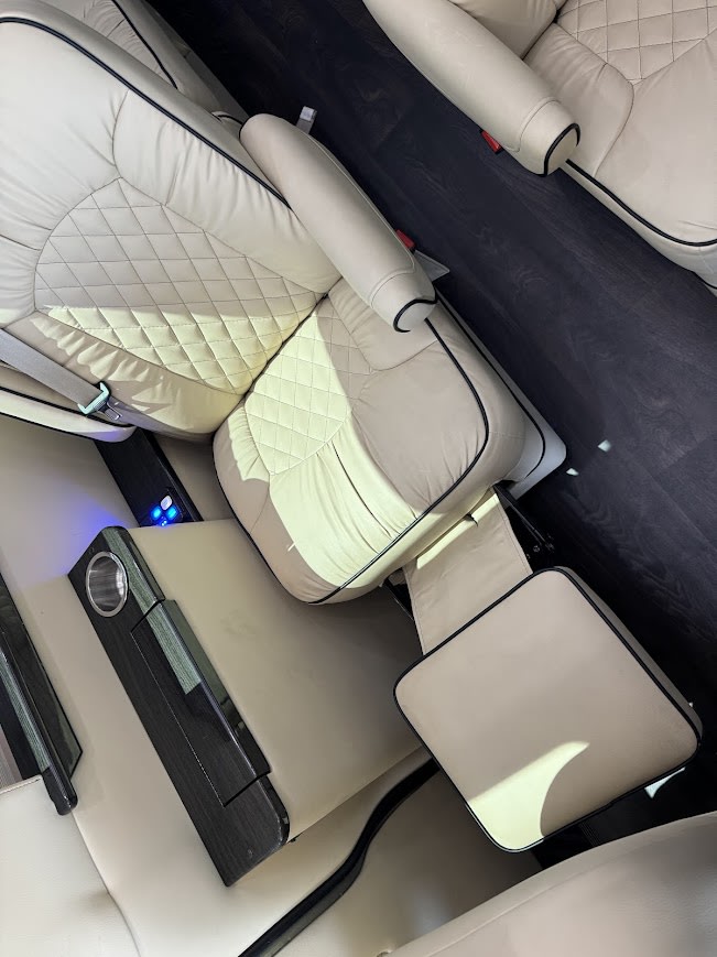 Luxury RV rental interior: beige quilted leather seats, dark wood floor, leg rest, & console. Comfort on the road! — photo 9