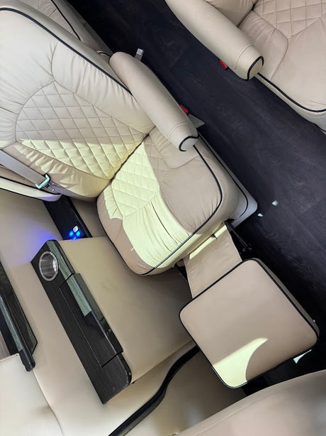 Luxury RV rental interior: beige quilted leather seats, dark wood floor, leg rest, & console. Comfort on the road!