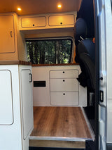 Modern RV rental interior: Clean white cabinets, wood paneling, ambient lighting, and a window view of trees.