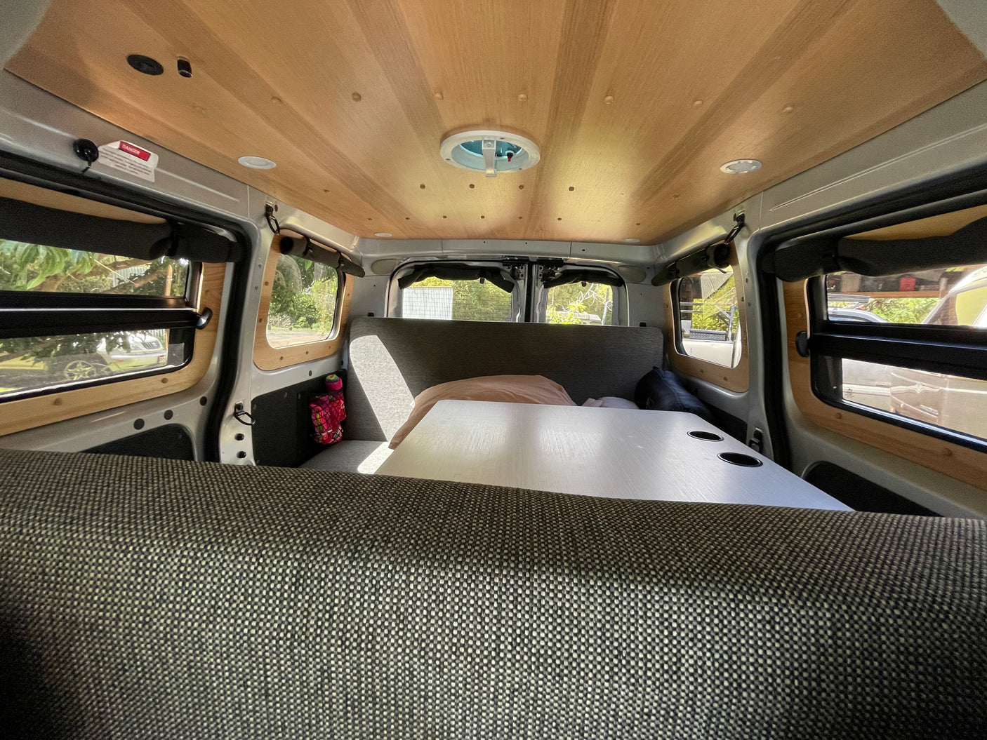Inside an RV rental camper van: wood-paneled ceiling with fan, central table with cupholders, and upholstered seating.
