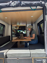 Woman focuses on laptop at a versatile table inside this modern RV rental, a comfy camper van providing a great mobile workspace.