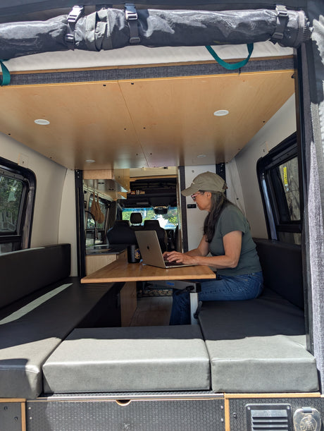 Woman focuses on laptop at a versatile table inside this modern RV rental, a comfy camper van providing a great mobile workspace.