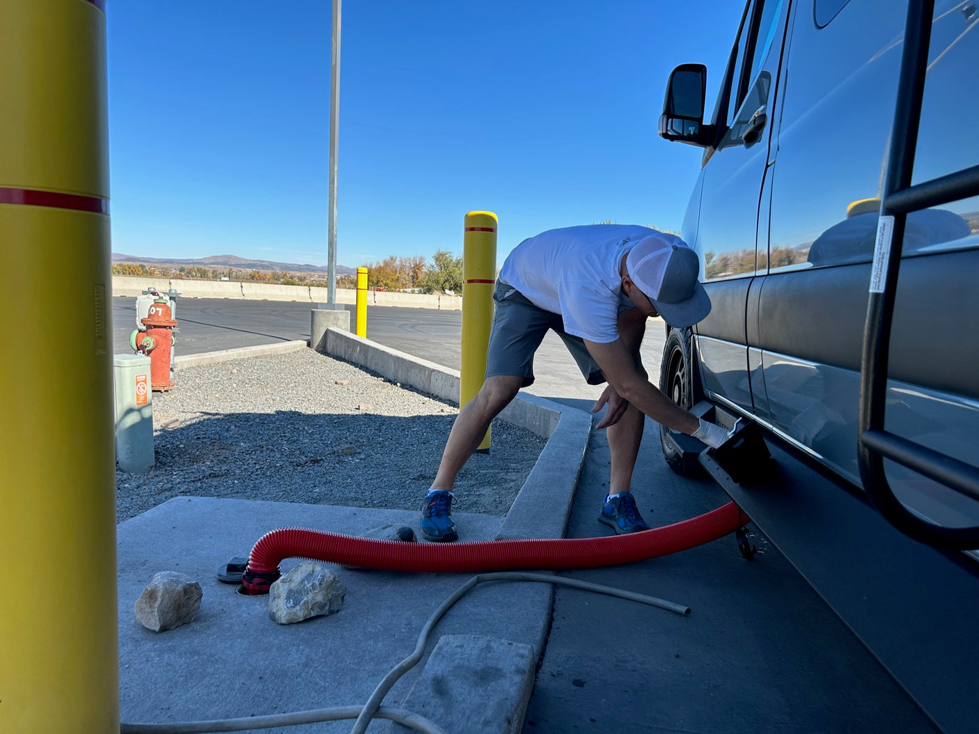 Man in gloves connects an RV rental to a dump station for waste disposal.