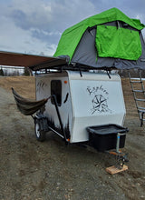 Compact RV rental: White teardrop camper with green rooftop tent, perfect for outdoor adventures.