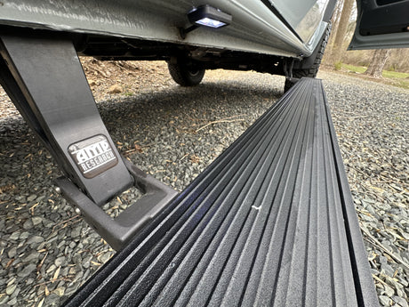An RV rental features extended AMP Research power steps with LED lighting, making entry easy on this gravel surface.