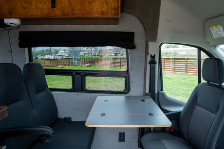 RV rental interior featuring a practical table, comfortable seating, and large windows overlooking a fenced yard.
