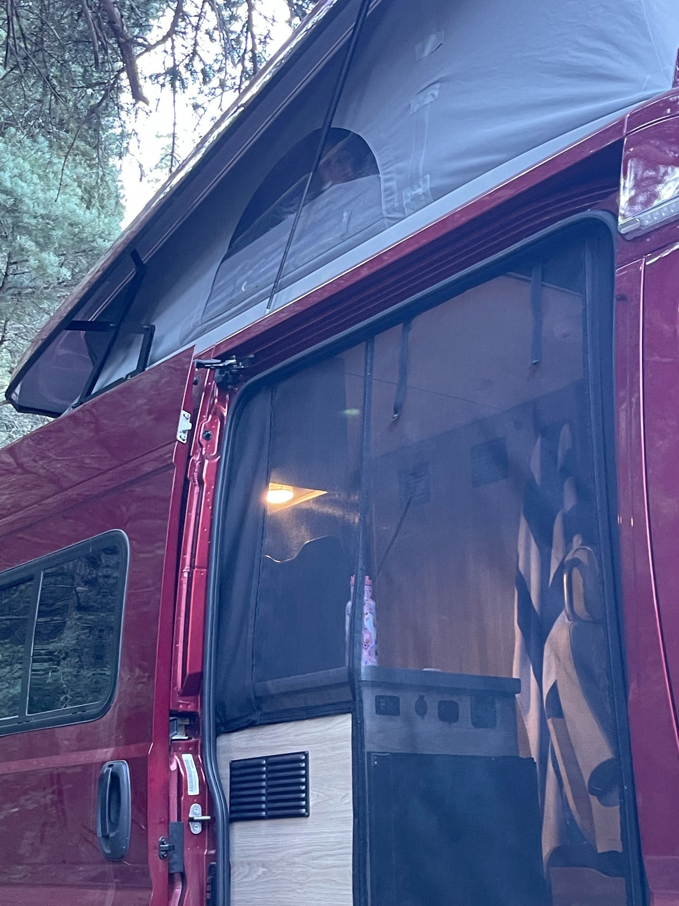 Enjoy an rv rental! This red camper van features an extended pop-top and screen door, with a glimpse of the illuminated interior. — photo 8