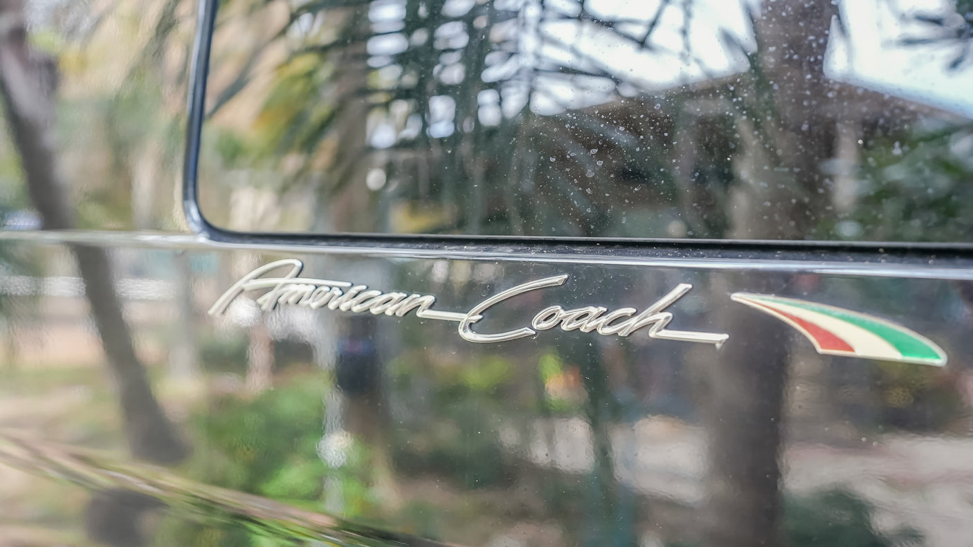 Close-up of a shiny 'American Coach' luxury RV emblem, featuring a red, white, green stripe. Explore premium rv rental.