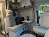 Modern camper van RV rental interior. Features light seating, fold-out table, overhead TV & storage for comfortable travel.