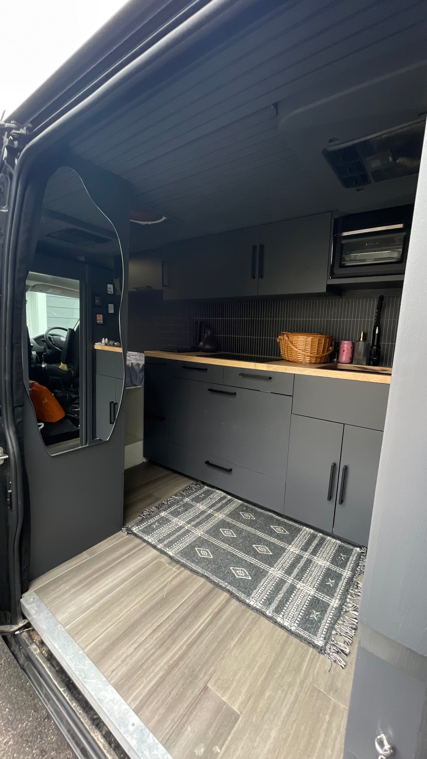Stylish RV rental interior: modern grey kitchen, wood counters, tiled backsplash, and mirror reflecting the front cabin.