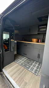 Stylish RV rental interior: modern grey kitchen, wood counters, tiled backsplash, and mirror reflecting the front cabin.