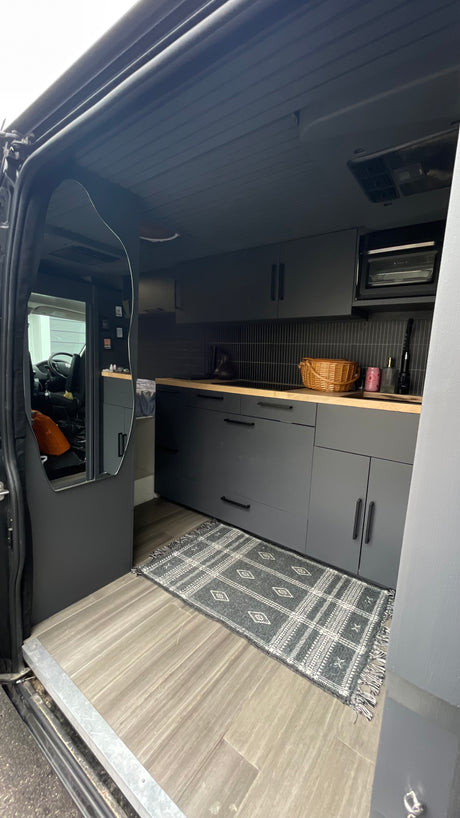 Stylish RV rental interior: modern grey kitchen, wood counters, tiled backsplash, and mirror reflecting the front cabin.