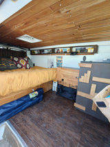 An rv rental camper van interior featuring a cozy bed, wooden slatted ceiling with skylight, and built-in storage.