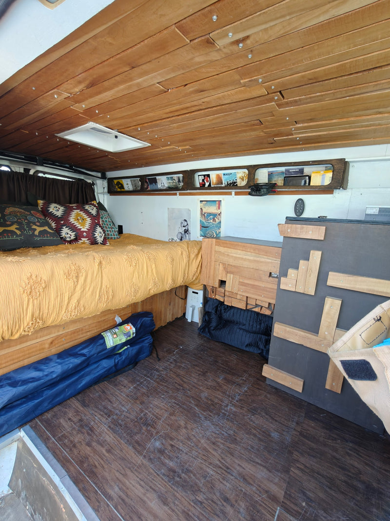 An rv rental camper van interior featuring a cozy bed, wooden slatted ceiling with skylight, and built-in storage. — photo 2