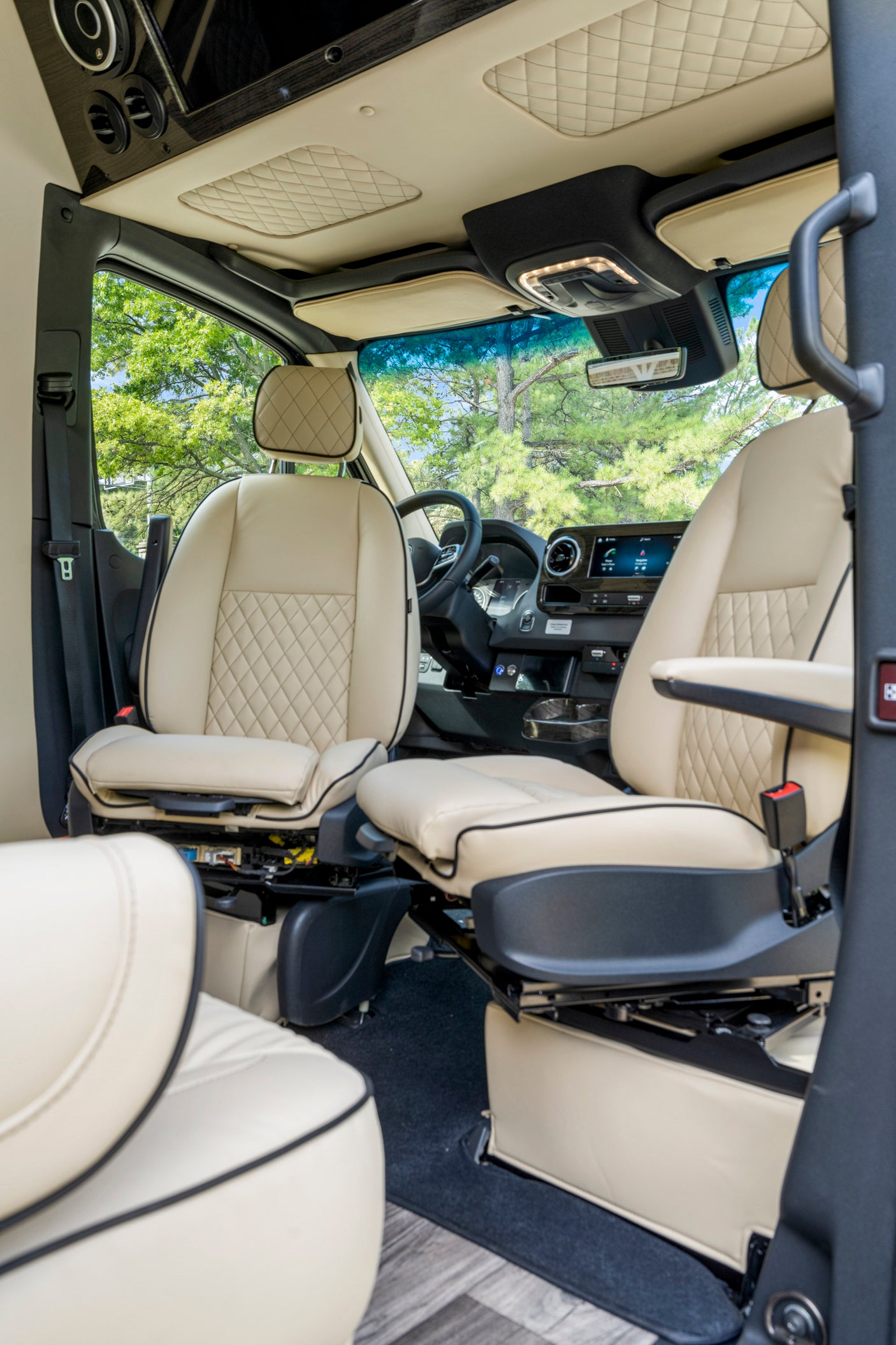 Luxurious cream leather interior of an RV rental van, featuring quilted seats, a modern dashboard, and lush outdoor views.