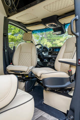 Luxurious cream leather interior of an RV rental van, featuring quilted seats, a modern dashboard, and lush outdoor views.