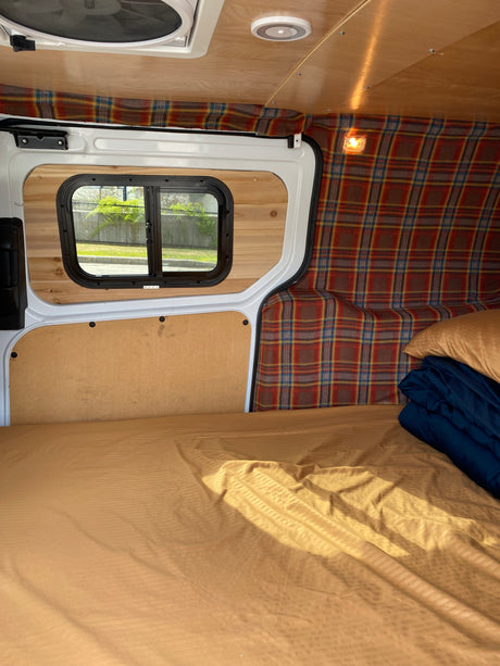Cozy RV rental interior with a bed, plaid decor, wood paneling, and a window view. Ideal for mobile living.