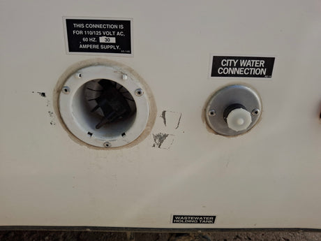 RV rental's external utility panel: 30A electrical input, city water connection, and wastewater tank label clearly visible.