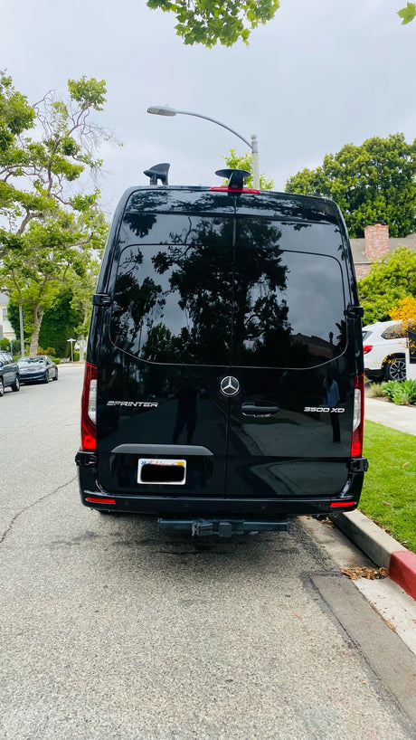 Rear view of a black Mercedes-Benz Sprinter 3500 XD van, often an RV rental, parked curbside on a residential street.