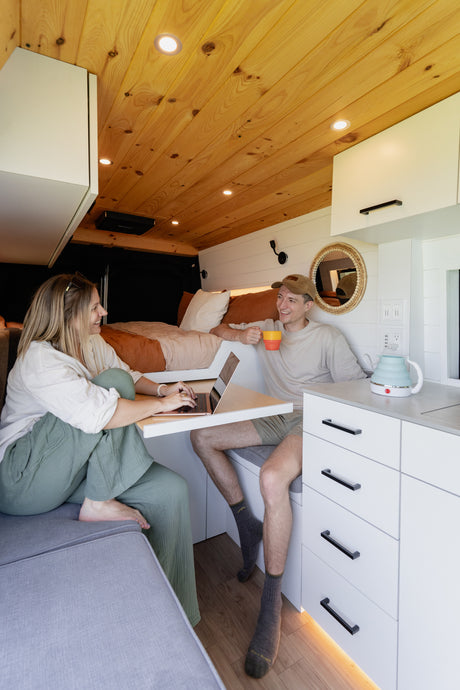 Cozy RV rental interior: A couple enjoys coffee & laptop work, embodying the perfect van life digital nomad setup.