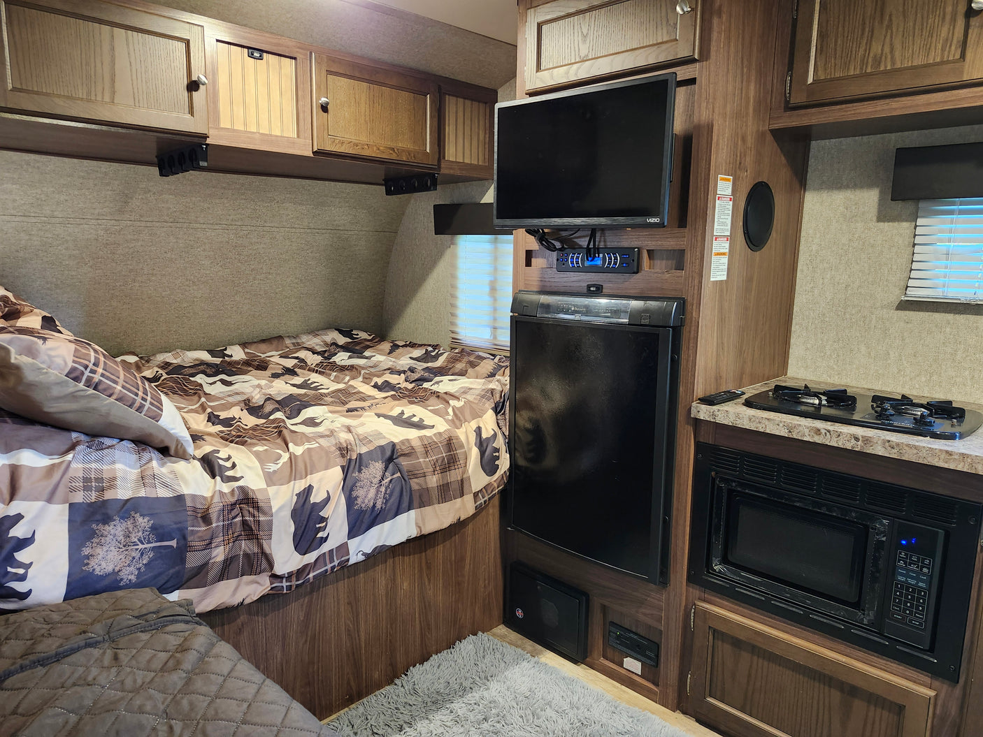 RV rental interior featuring a compact bedroom, kitchen area with stove & microwave, fridge, TV, and storage.