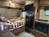 RV rental interior featuring a compact bedroom, kitchen area with stove & microwave, fridge, TV, and storage.