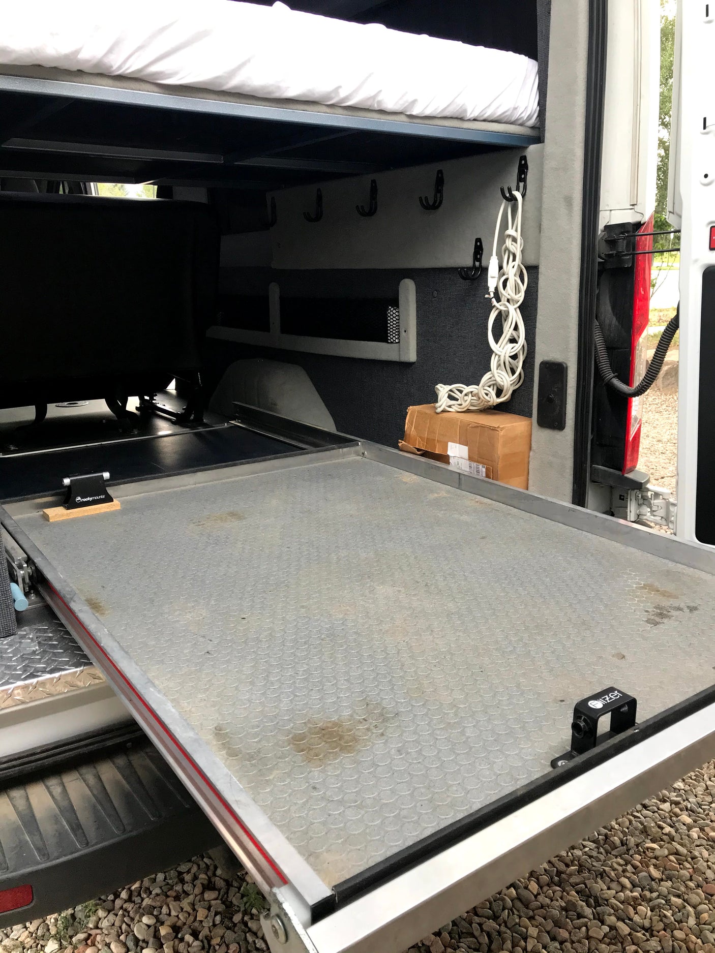 RV rental interior showing an organized sleeping area with a bed, hanging hooks, and a heavy-duty pull-out tray.