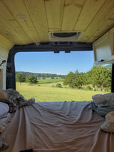 Experience an rv rental! Cozy camper van bed with a stunning view of a green vineyard, hills, and clear sky. Relaxing travel.