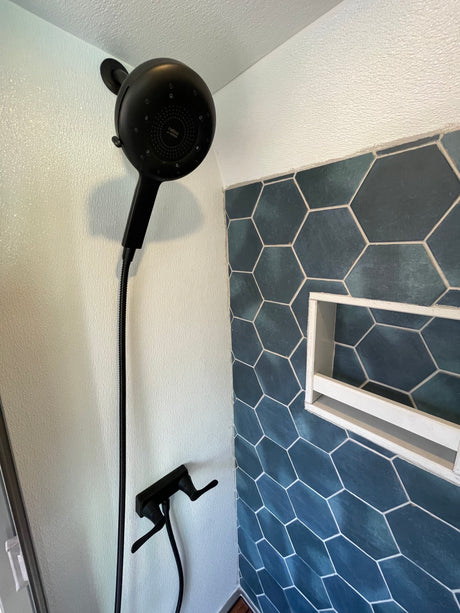 Modern RV rental shower with hexagon tiles, a built-in niche, and a sleek black Nebia showerhead.