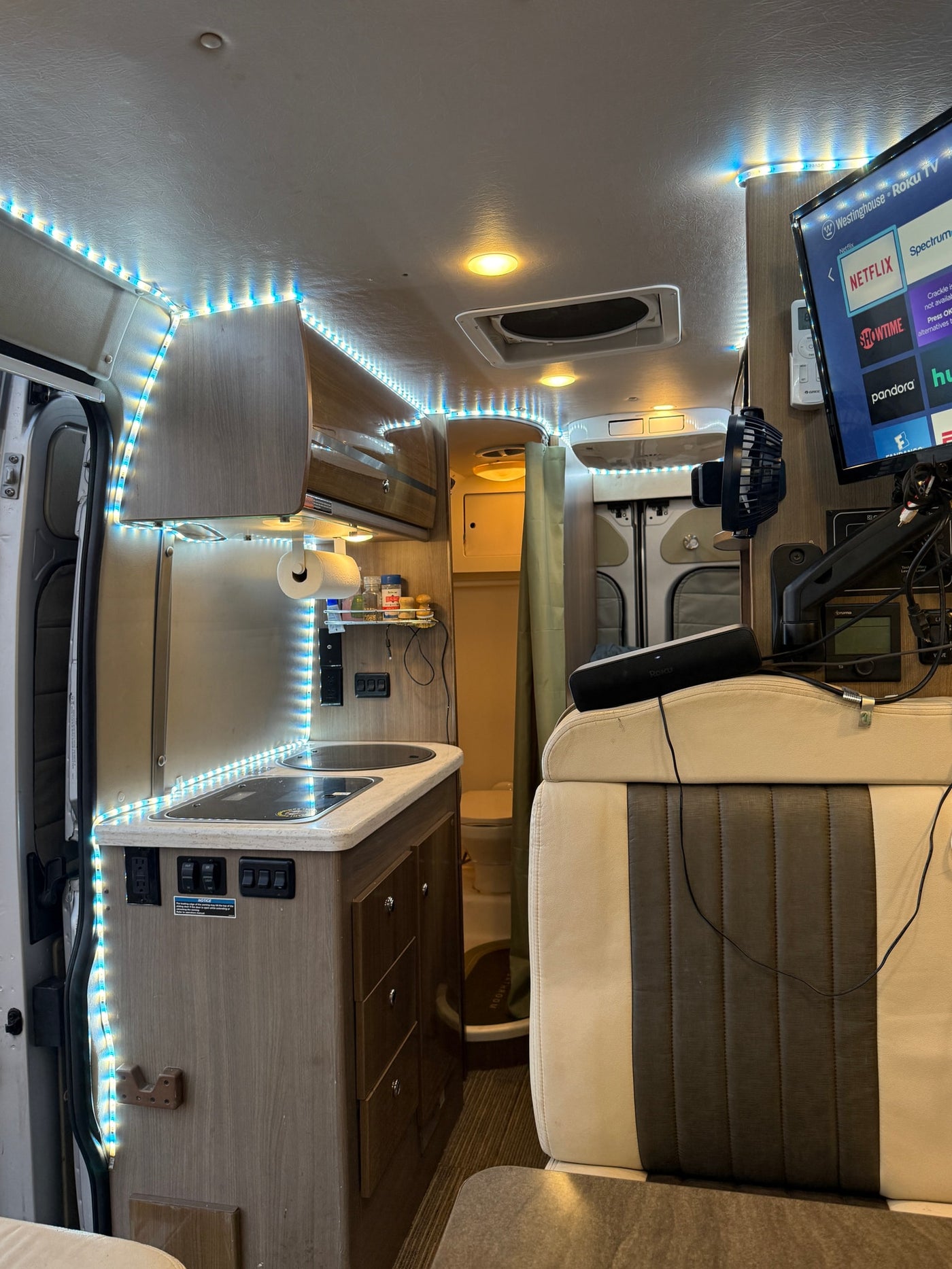 This RV rental interior features a functional kitchenette, a mounted TV for entertainment, and colorful LED strip lighting. — photo 9