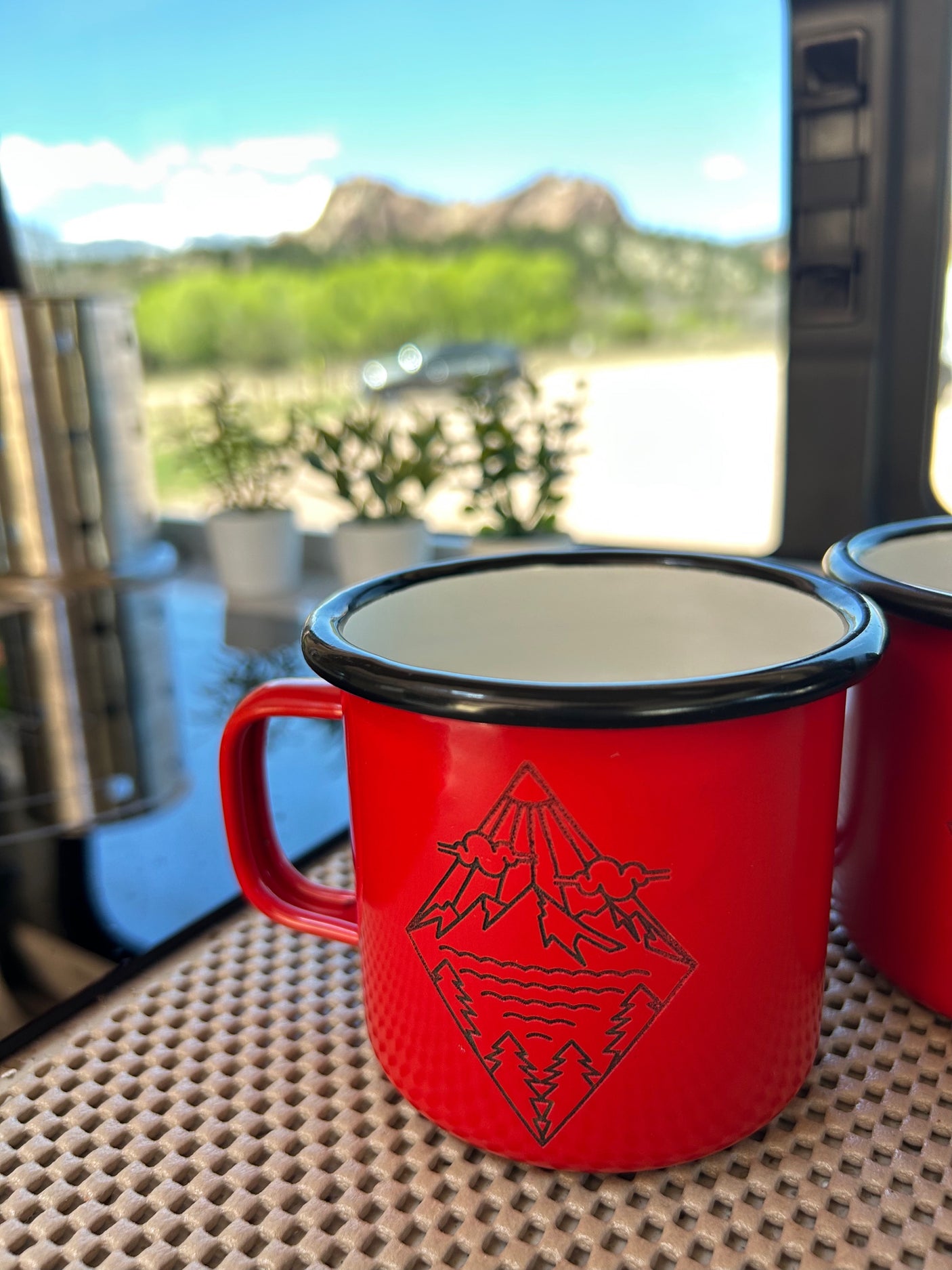 Scenic RV rental view: red enamel mugs ready for adventure, overlooking mountains & greenery.