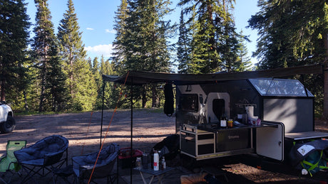 Experience the outdoors! This RV rental, a Teton camper trailer, with an outdoor kitchen, is set up at a serene forest campsite.