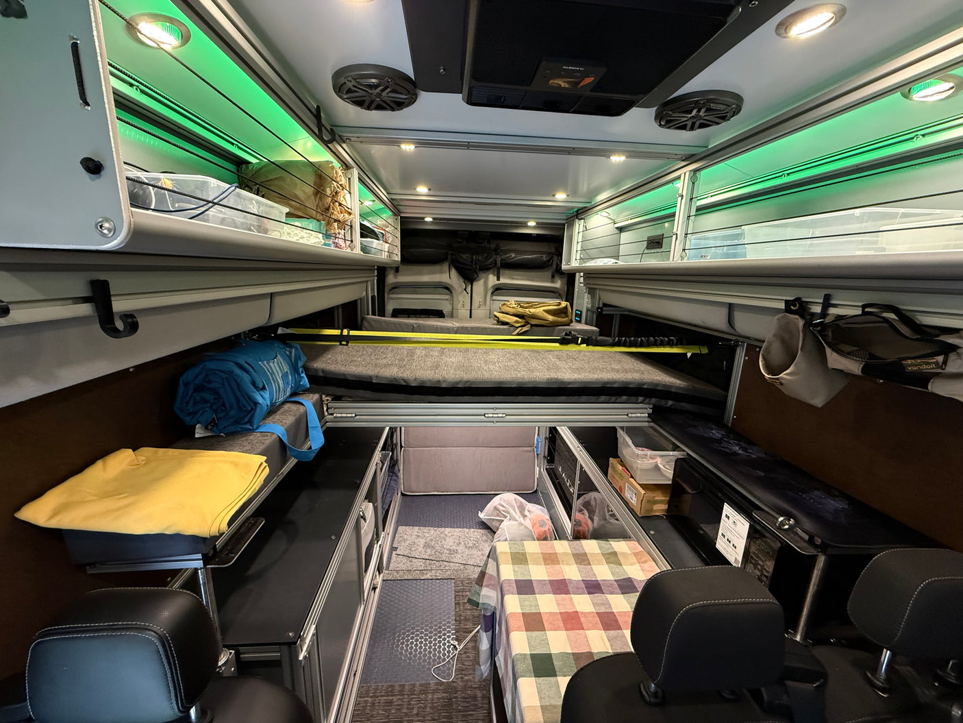RV rental interior features a modular bed, overhead green-lit storage, and seating, offering a compact living space.