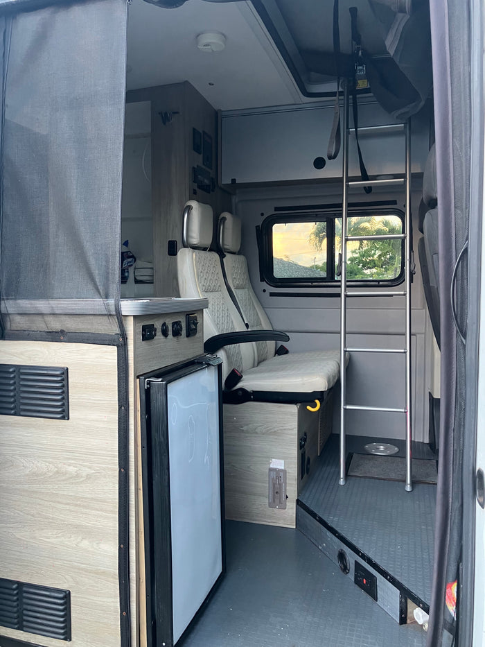 Experience comfort in this RV rental interior: light wood cabinetry, cream seats, compact fridge, and ladder access.