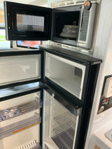 RV rental kitchen featuring an open microwave, with a plate inside, above an open freezer and refrigerator unit. Control panel visible.