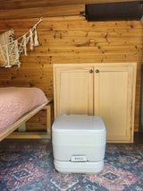RV rental interior: cozy bed, wooden walls, and essential portable toilet for comfortable van life adventures.