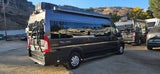 Dark gray Tellaro Ram Promaster RV rental camper van, equipped with a bike rack, in a sunny, dusty lot.