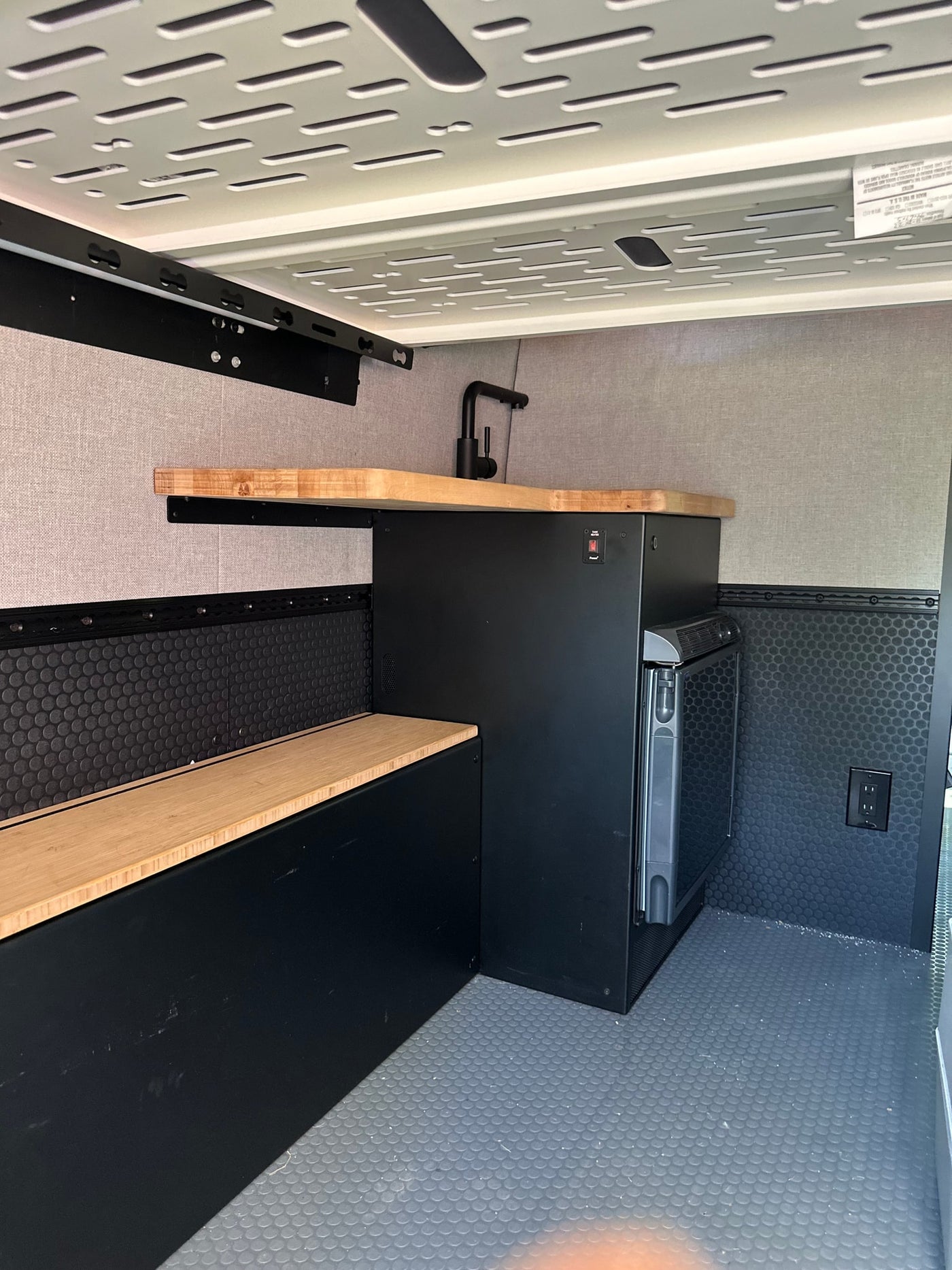 Compact RV rental interior featuring a kitchenette with wood counter, sink, fridge, and built-in bench. — photo 12