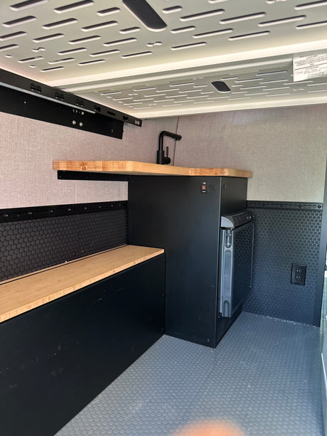 Compact RV rental interior featuring a kitchenette with wood counter, sink, fridge, and built-in bench.